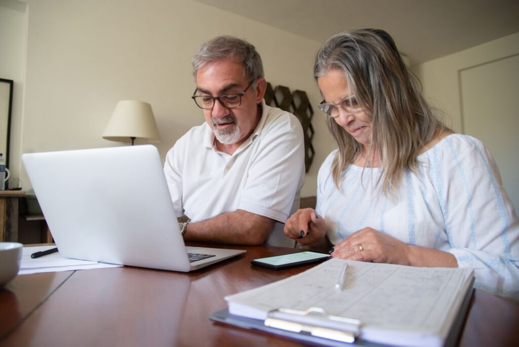 Senior couple at a desk reviewing retirement-income documents with a laptop and smartphone, illustrating the account-based pension versus annuity decision Véurr Financial Planning helps Canberra pre-retirees navigate.