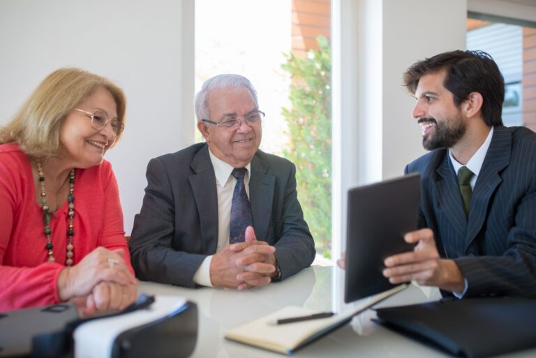Financial adviser meeting with an older couple over documents and a tablet in a bright, neutral office.