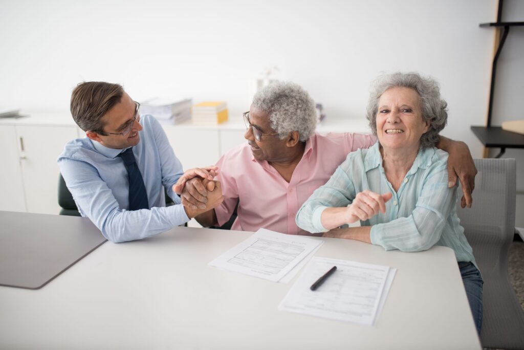 Senior couple discussing redundancy and retirement paperwork with a financial adviser in a bright office.