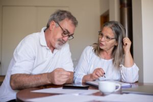 Couple in their mid-fifties reviewing superannuation paperwork together at a table in a bright, neutral room.