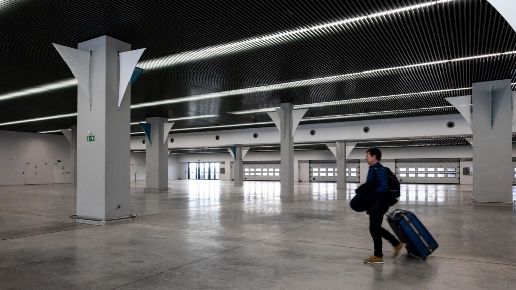 A lone traveller walking through an empty modern airport terminal with a suitcase, on the way to an overseas posting
