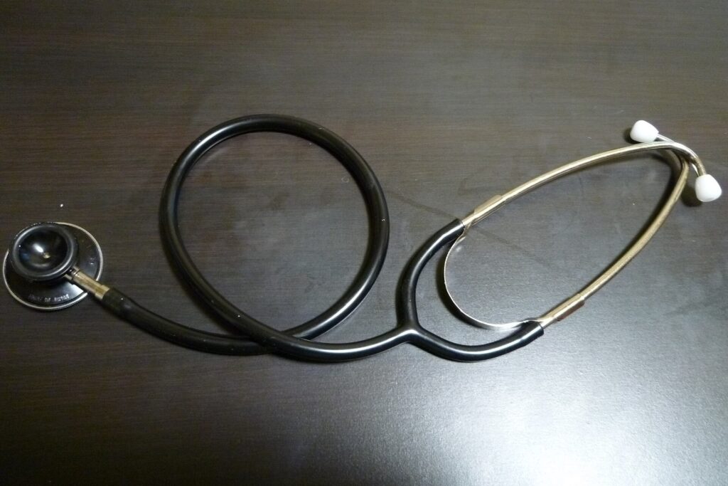 A black stethoscope lying coiled on a dark wooden desk.