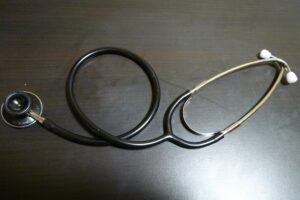 A black stethoscope lying coiled on a dark wooden desk.